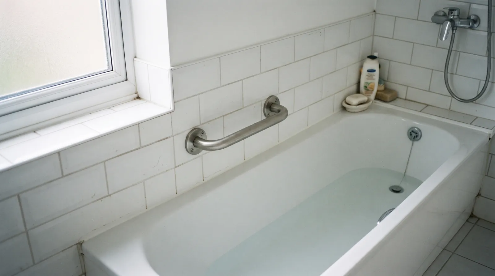 A newly fitted grab rail beside a bathtub in a plain, well-lit bathroom.